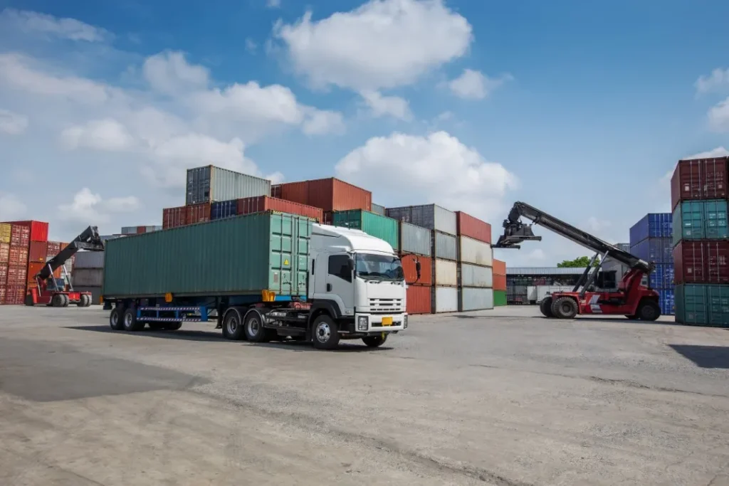 Fotografía de un camion blanco a lado de varios contenedores apunto de llenarlo de productos para realizar un servicio FTL